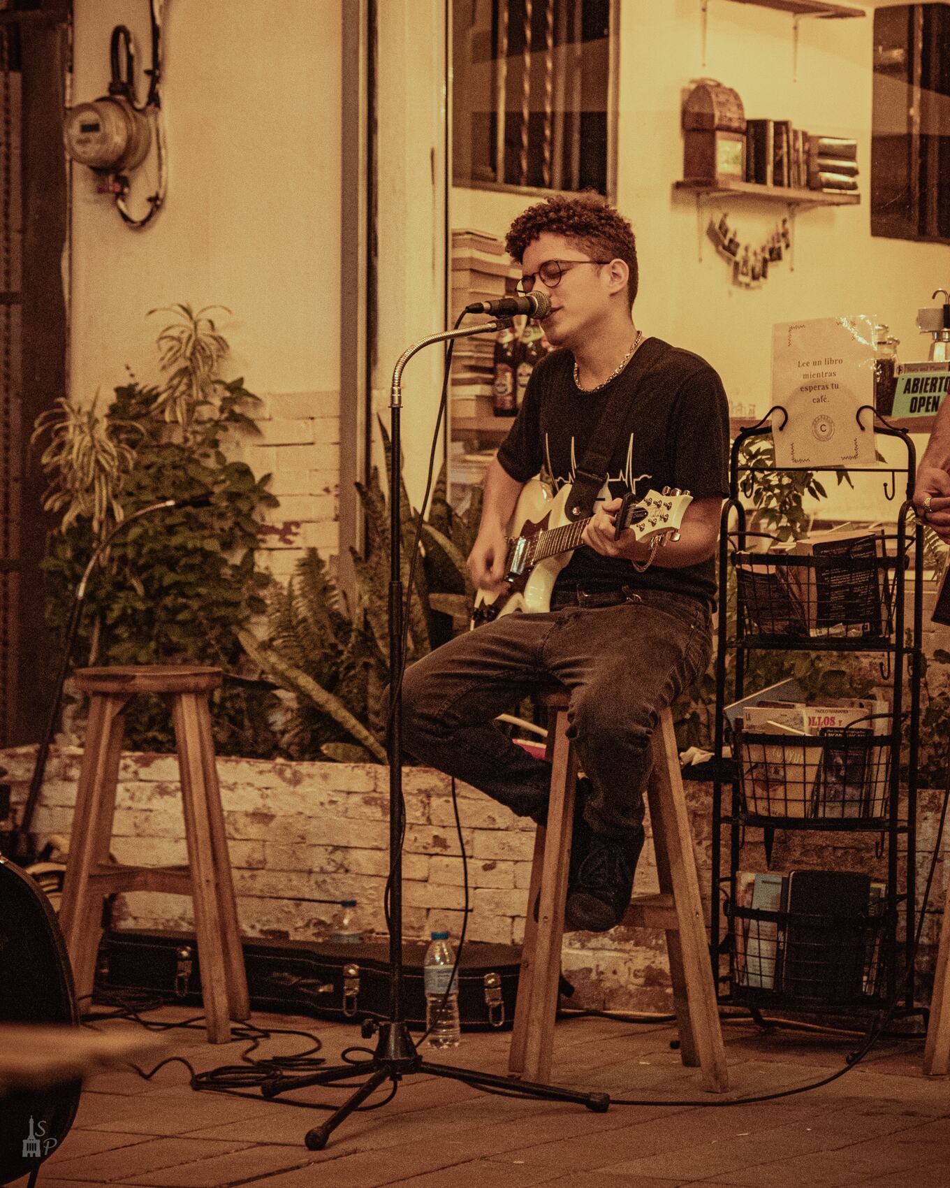 El Científico tocando guitarra eléctrica sentado en un taburete, en un café